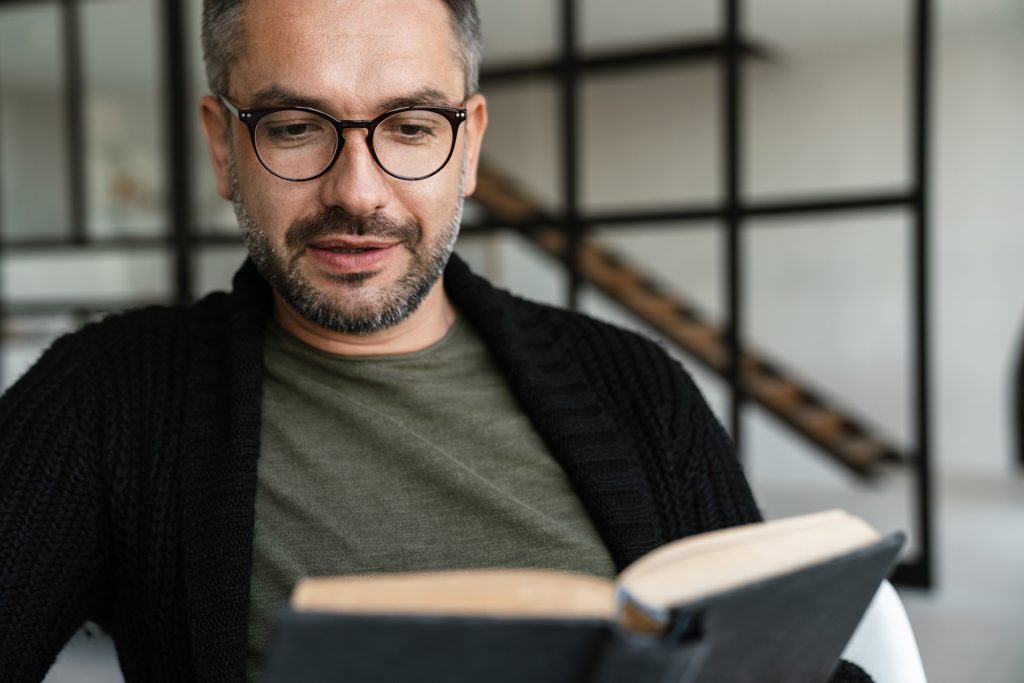 Confident middle-aged man reading a men's health book at home, focusing on personal wellbeing